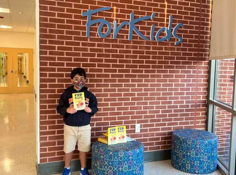 A young child stands with a book he authored in front of a non-profit