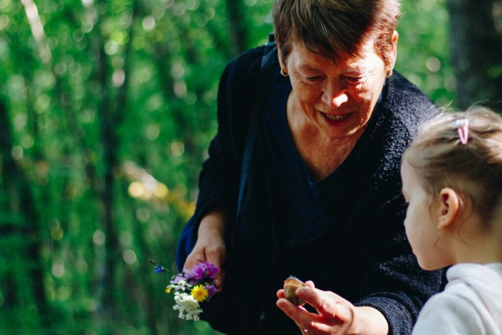 Older woman holds flowers out to a young girl.