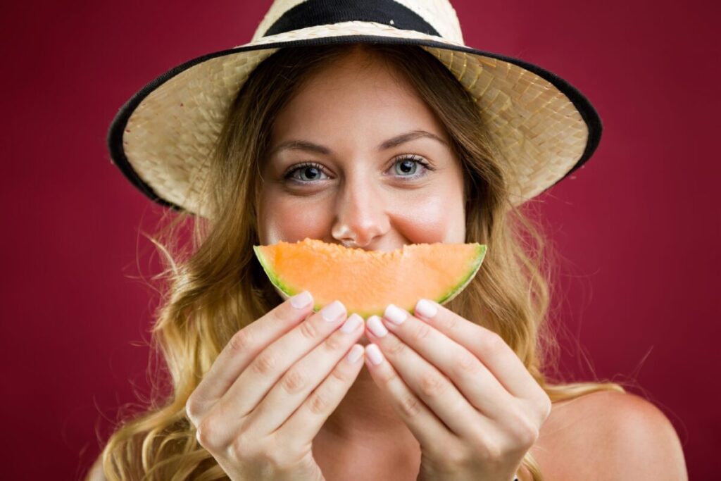 Portrait of beautiful young woman in bikini eating melon. Isolated on red.