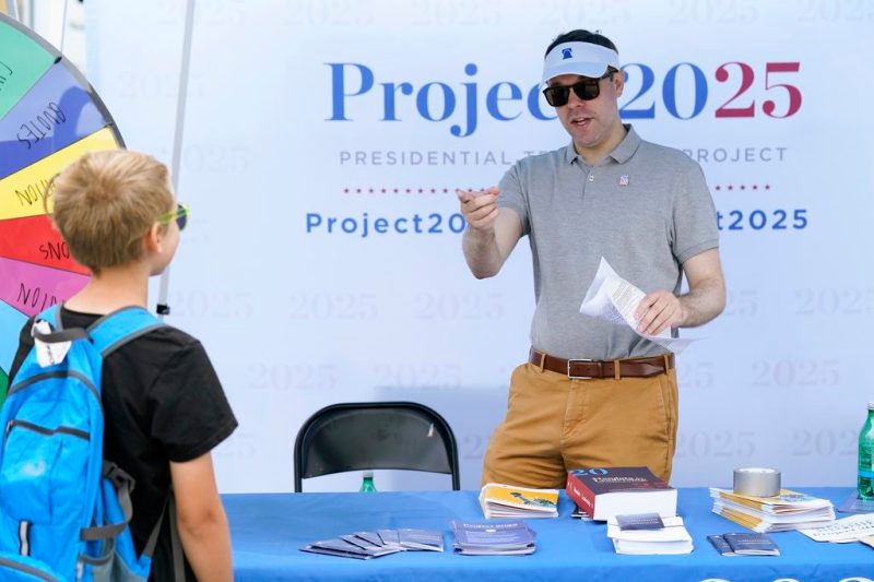 Spencer Chretien, right, talks to a young fairgoer at the Project 2025 tent at the Iowa State Fair, Aug. 14, 2023, in Des Moines, Iowa. With more than a year to go before the 2024 election, a constellation of conservative organizations is preparing for a possible second White House term for Donald Trump. The Project 2025 effort is being led by the Heritage Foundation think tank. (AP Photo/Charlie Neibergall)