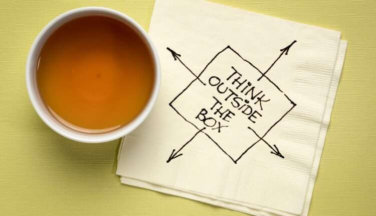 "think outside the box" written on a white napkin against a green background.