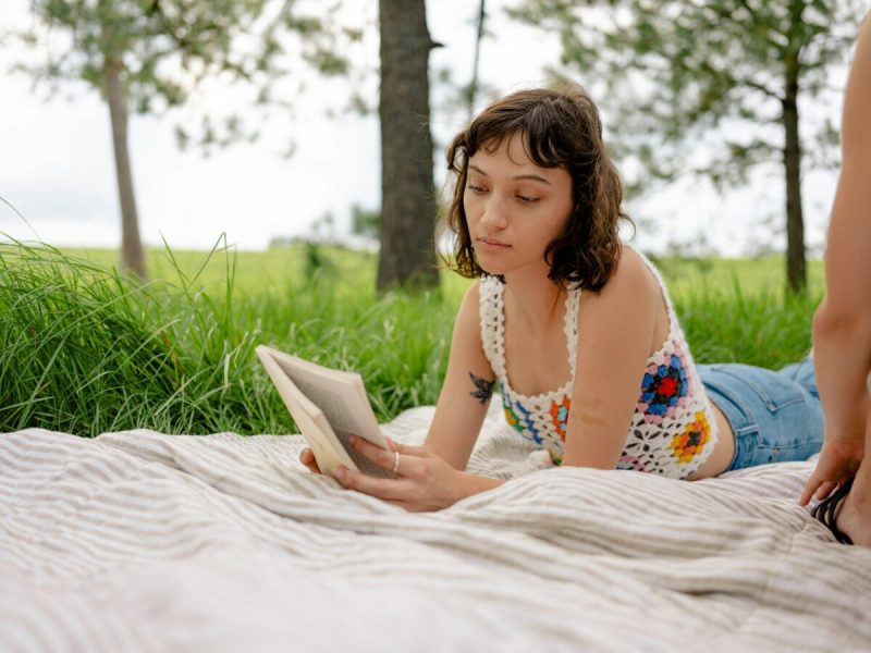 a white woman on her stomach on a blanket outside reading a book by virginia authors