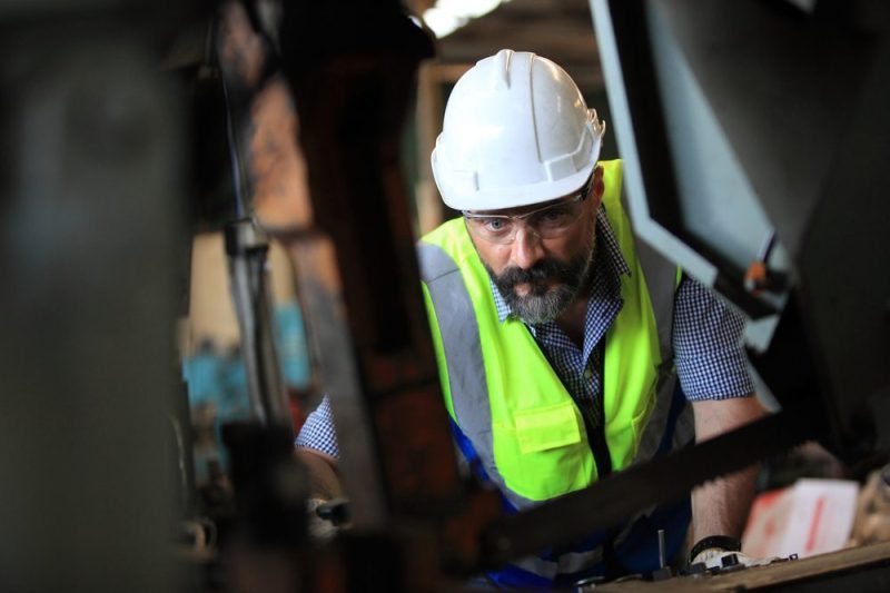 Photo of a man in a work helmet and vest doing a job of sorts.