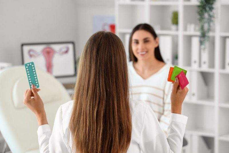Photo of a woman holding up condoms in one hand and birth conrtol pill in another to show another woman.