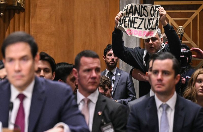 A protestor holds up a sign as US Secretary of State Marco Rubio testifies during a Senate Foreign Relations Committee hearing to examine US policy towards Venezuela on Capitol Hill in Washington, DC, January 28, 2026. US military raided Caracas on January 3 and seized Nicolas Maduro, a longtime leftist nemesis of Washington, and his wife, Cilia Flores.
