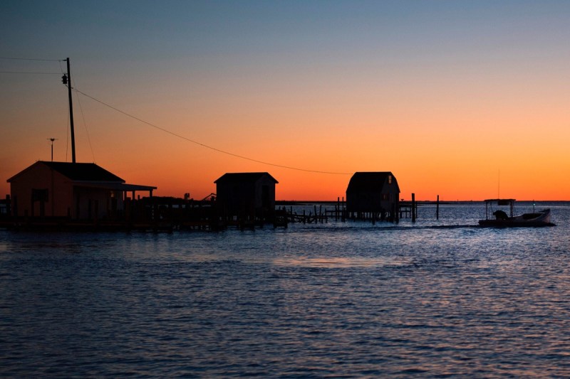 The sun rises while a waterman passes crab shanties as he sets out for the day in Tangier, Virginia
