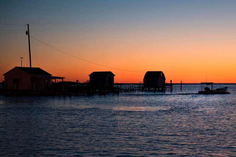 The sun rises while a waterman passes crab shanties as he sets out for the day in Tangier, Virginia